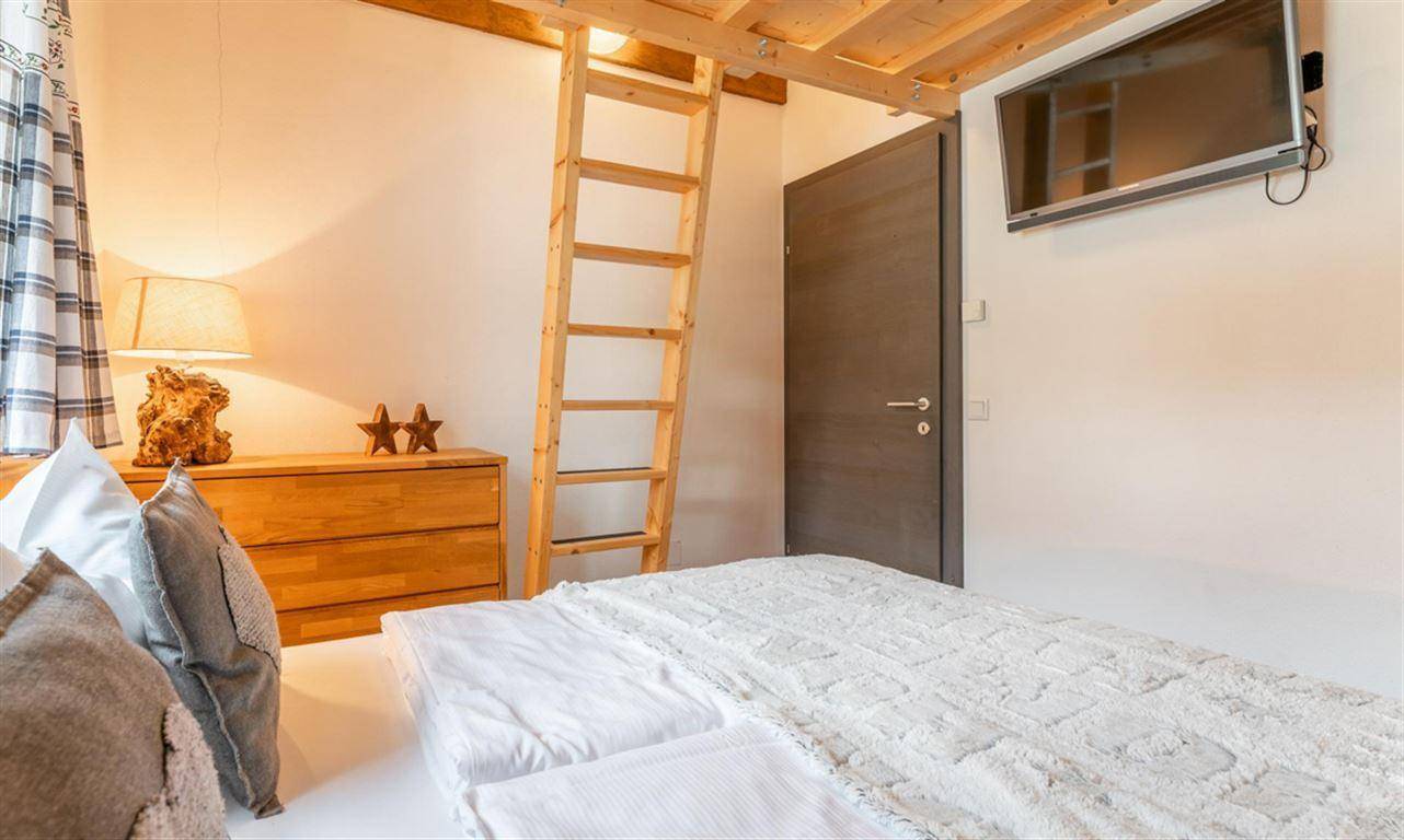 Schlafzimmer mit Doppelbett, Fernseher und Leiter zu einem zusätzlichen Schlafbereich.