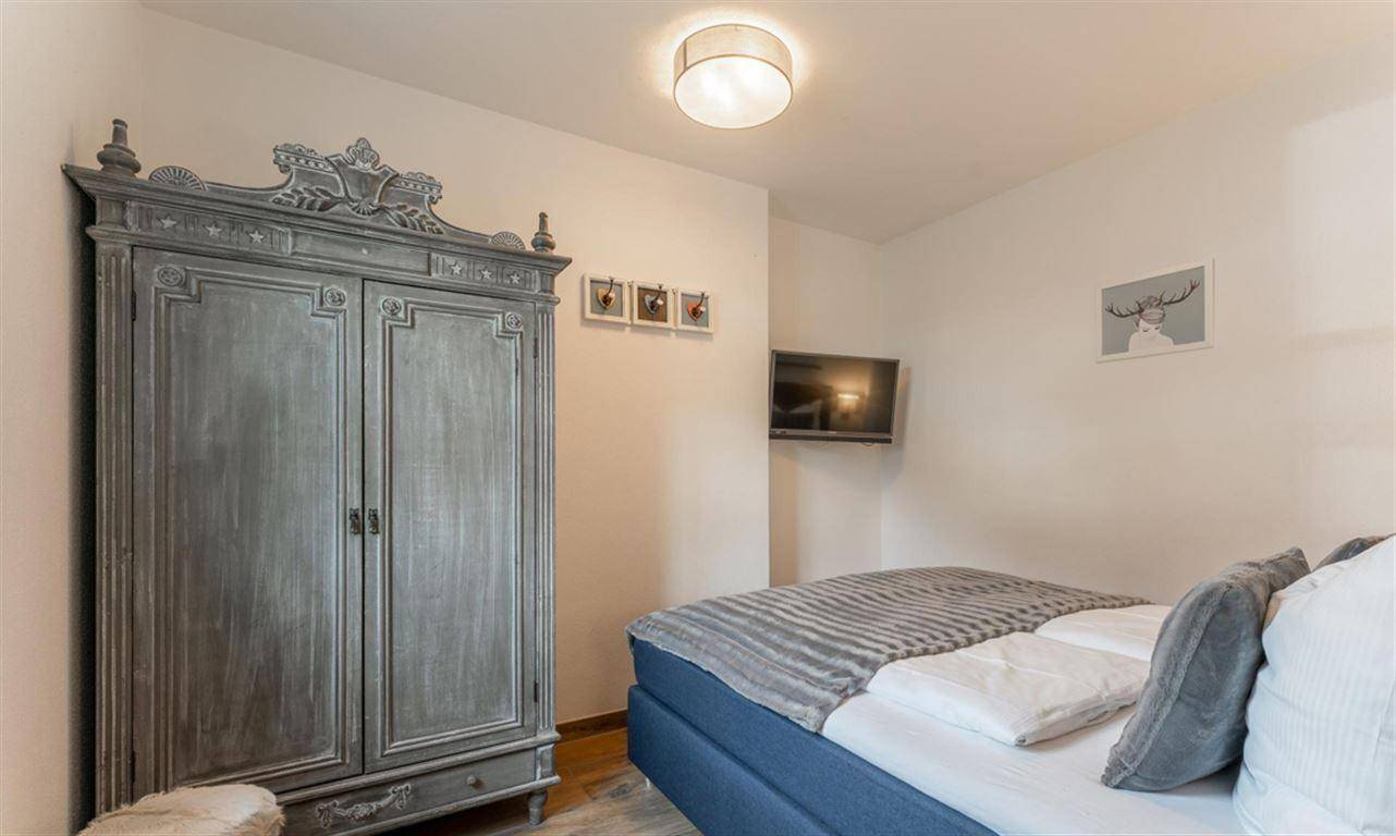 Schlafzimmer mit Doppelbett, antikem Kleiderschrank und Fernseher für Komfort.