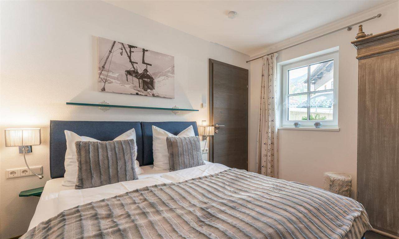Gemütliches Schlafzimmer mit Doppelbett, Holzschrank und Fenster mit Bergblick.