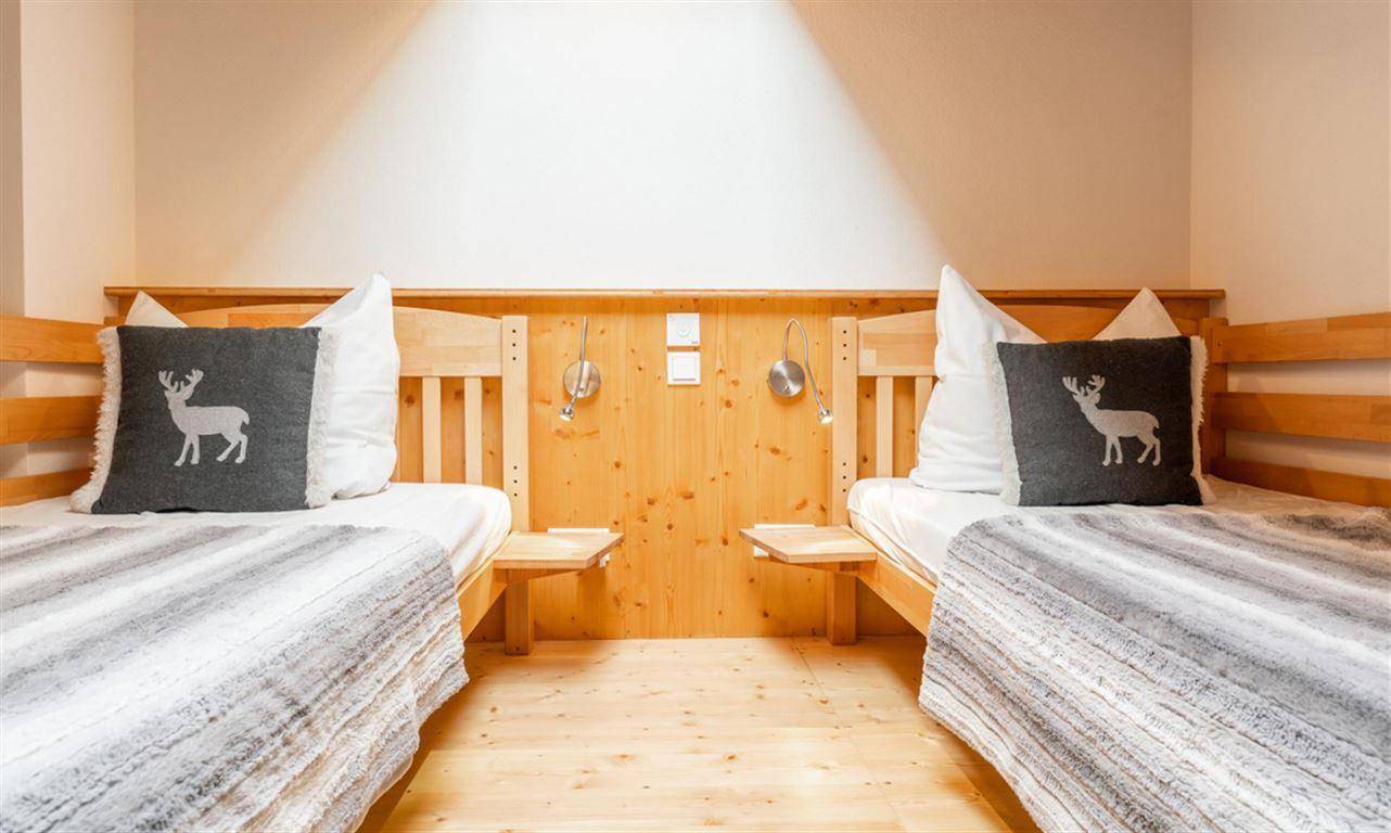 Schlafzimmer mit zwei Einzelbetten, Holzvertäfelung und alpiner Dekoration für Gäste.