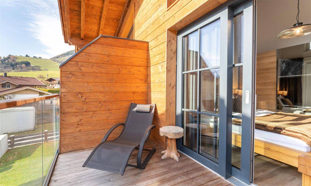 Gemütlicher Balkon mit Liegestuhl, Holzwänden und Blick ins Grüne.
