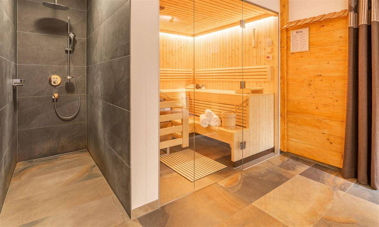 Modernes Badezimmer mit großer Dusche und angrenzender Sauna für Wellnessmomente.