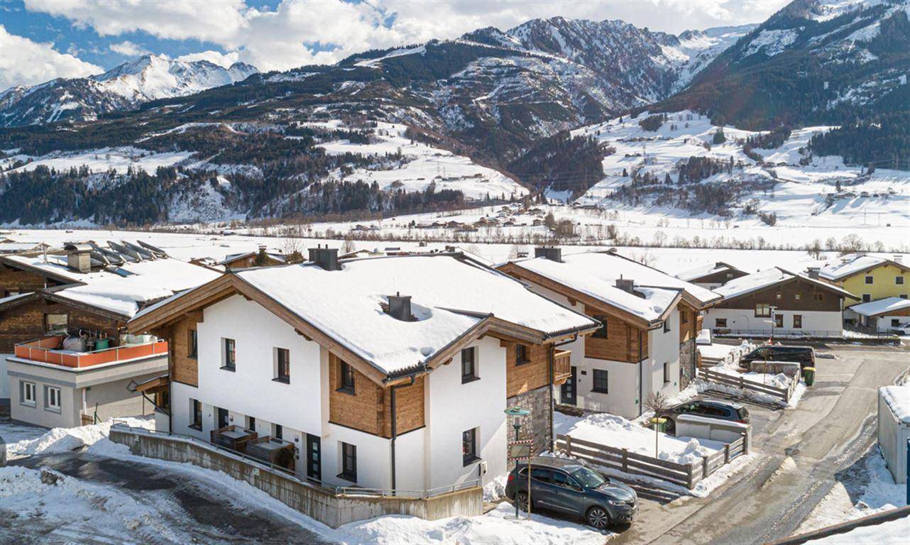 Luftaufnahme einer Chalet-Siedlung in einer malerischen, verschneiten Berglandschaft.