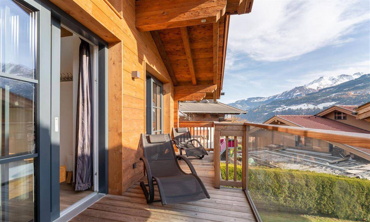 Sonniger Balkon mit Holzboden, Glasgeländer und beeindruckendem Bergblick.
