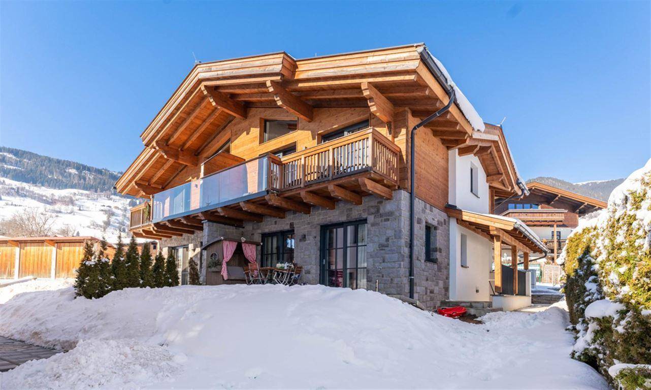 Modernes Chalet-Gebäude mit Holzfassade und Steinmauern in verschneiter Winterlandschaft.