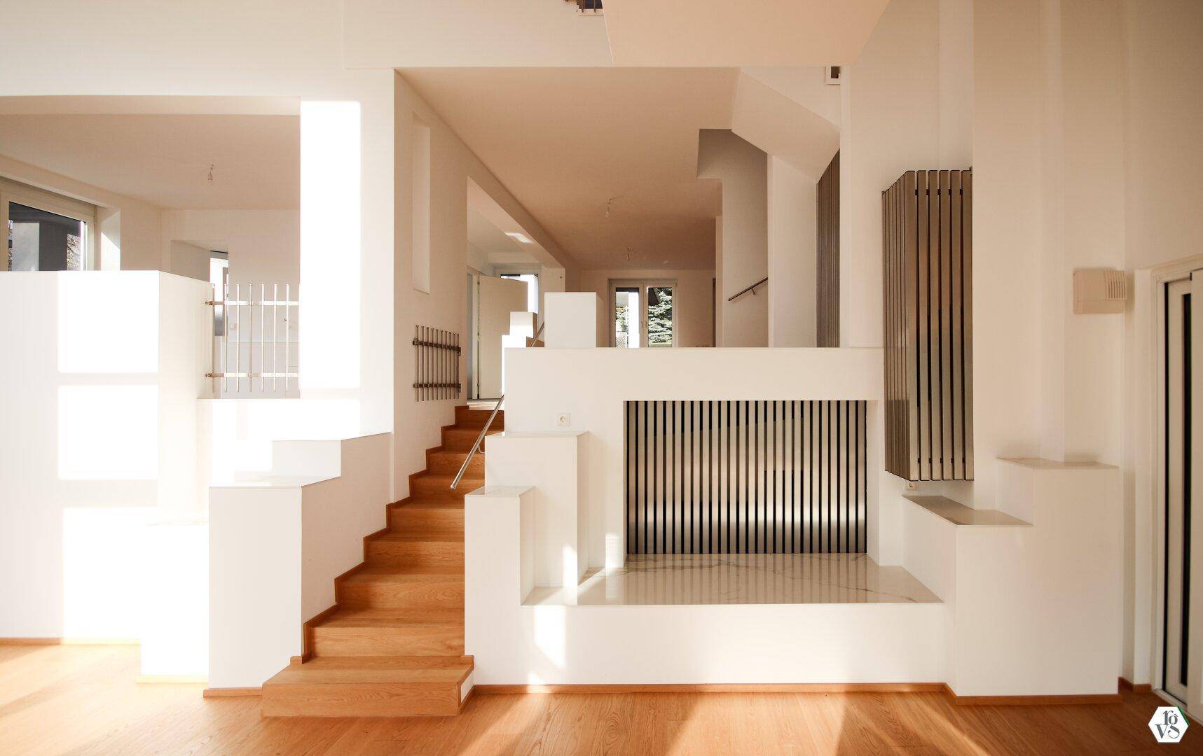 Heller, offener Wohnbereich mit Holztreppe und modernen Designelementen, lichtdurchflutet durch große Fenster.