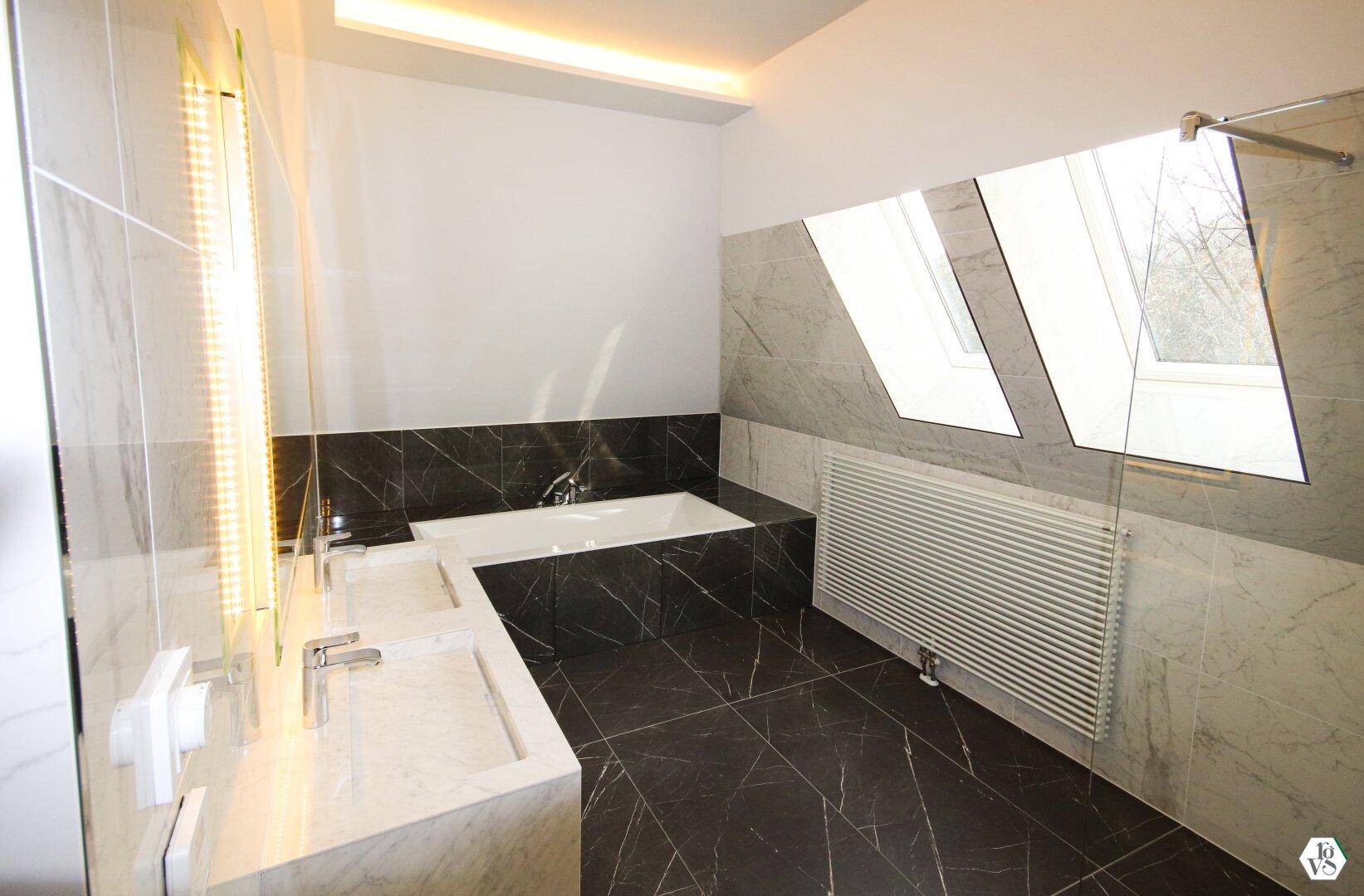 Elegantes Badezimmer mit Badewanne, modernen Armaturen und Dachfenstern, die für natürliches Licht sorgen.