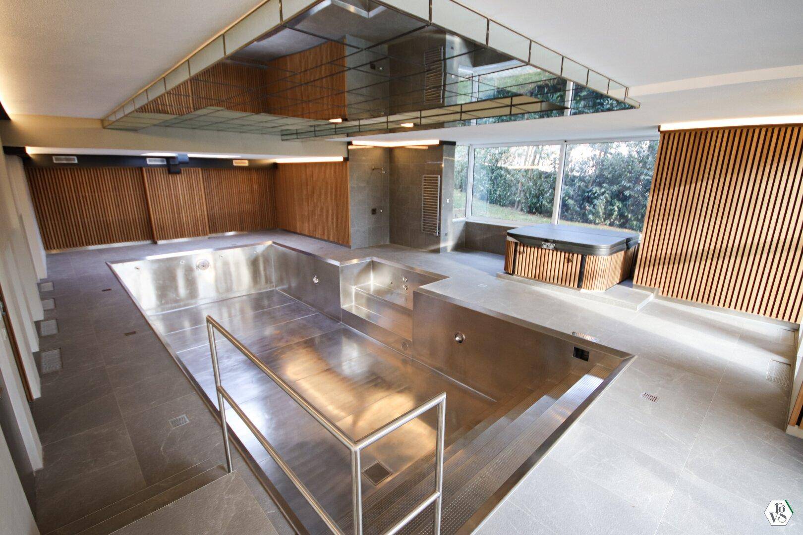 Exklusiver Wellnessbereich mit großem Innenpool aus Edelstahl und integriertem Whirlpool, umgeben von Holzverkleidungen.