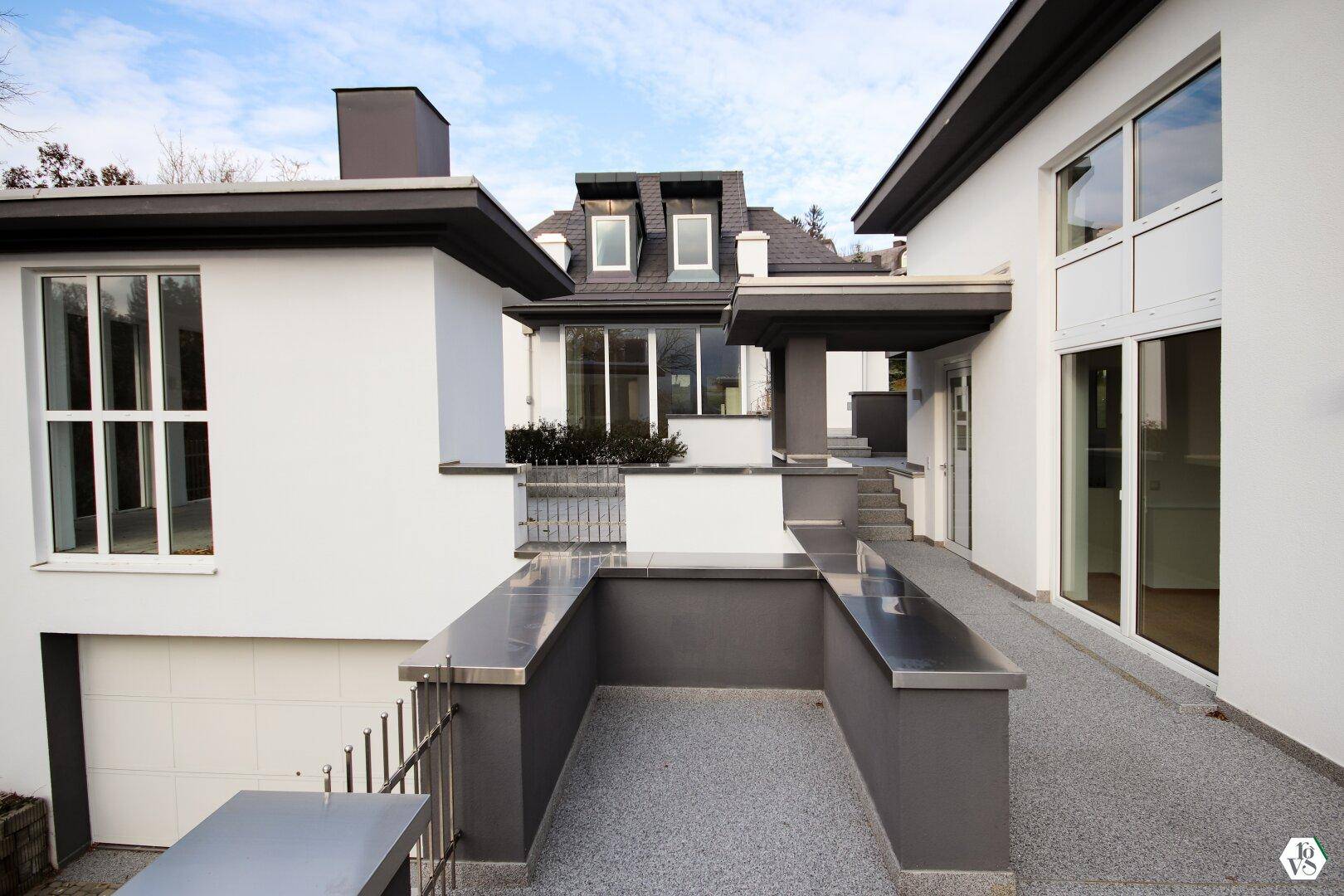 Seitlicher Zugang zur Villa mit Rampe und Treppen, umgeben von moderner Architektur und großen Fenstern.