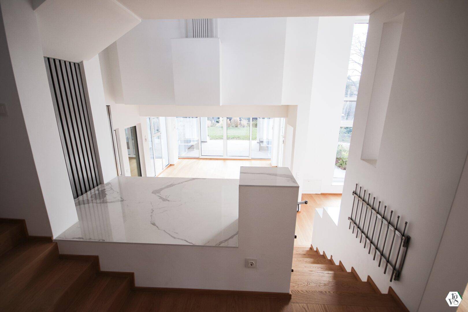 Blick von oben auf den offenen Wohnbereich mit hohen Decken und großen Fensterfronten, die den Raum erhellen.