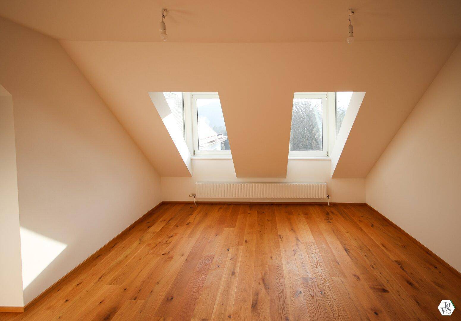 Helles Schlafzimmer im Dachgeschoss mit schrägen Wänden und zwei großen Dachfenstern, die viel Licht spenden.