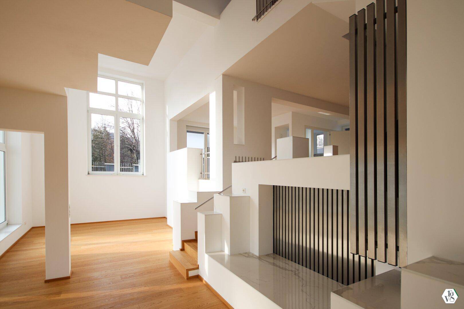 Lichtdurchfluteter Wohnbereich mit eleganten Treppen und hohen Fenstern, die viel Tageslicht hereinlassen.