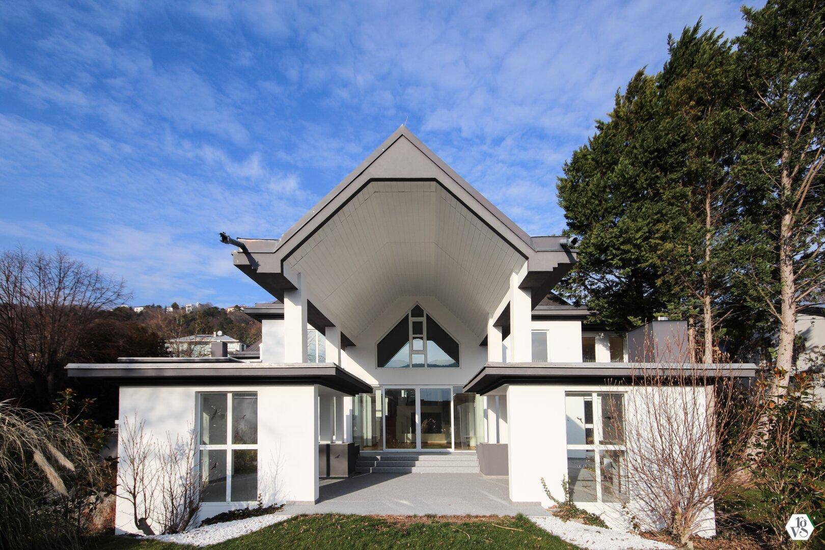 Beeindruckende moderne Villa mit markantem Giebel und großen Fenstern unter strahlend blauem Himmel.