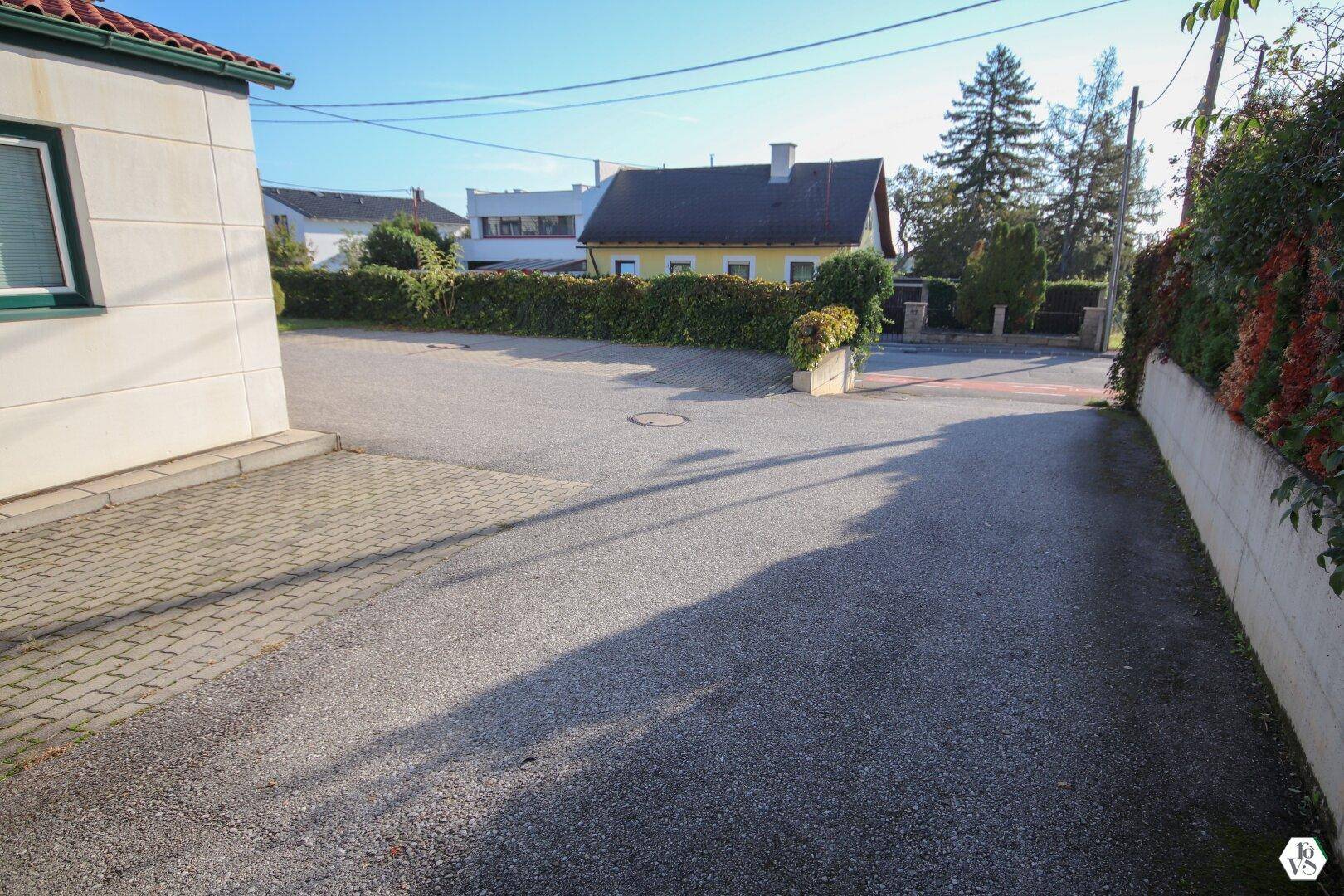 Zufahrtsstraße mit gepflasterten Bereichen und Blick auf umliegende Wohnhäuser und Grünflächen.