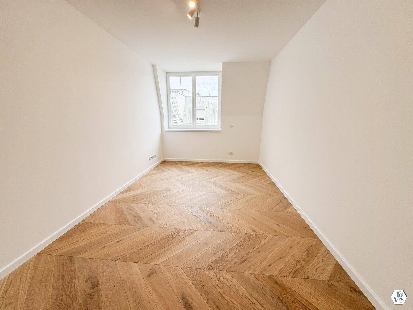 Heller Raum mit weiß gestrichenen Wänden und elegantem Fischgrät-Parkettboden.