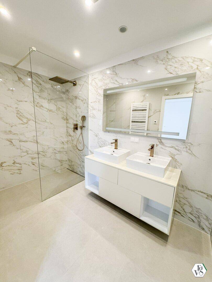 Helles Badezimmer mit zwei Waschbecken, großem Spiegel und begehbarer Dusche in Marmoroptik.