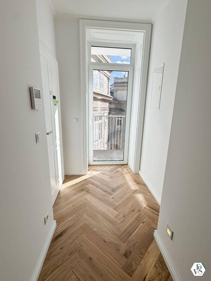 Heller Flur mit Fischgrätparkett und Zugang zu einem französischen Balkon, sorgt für einladendes Ambiente.