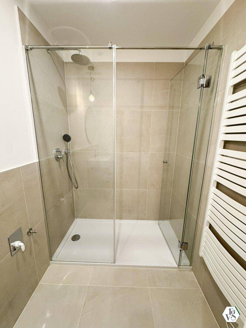 Geräumige, ebenerdige Dusche mit Glasabtrennung und Regenbrause in modernem Badezimmerdesign.