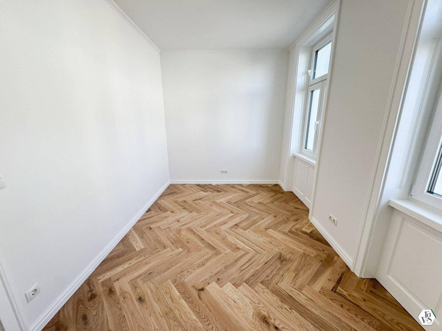 Renoviertes Zimmer mit hellem Fischgrätparkett und großen Fenstern, bereit zum Einzug und individuell gestaltbar.
