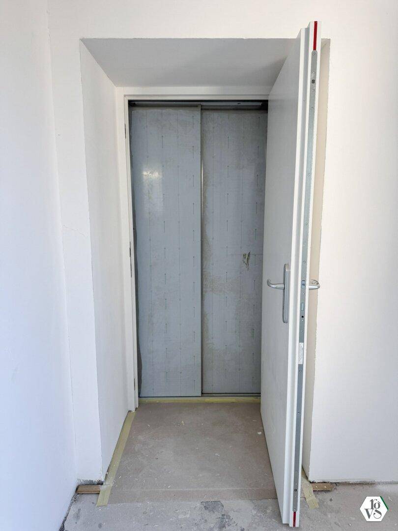 Eingangsbereich zu einem Aufzug mit weißen Wänden und Betonboden, noch im Bau.