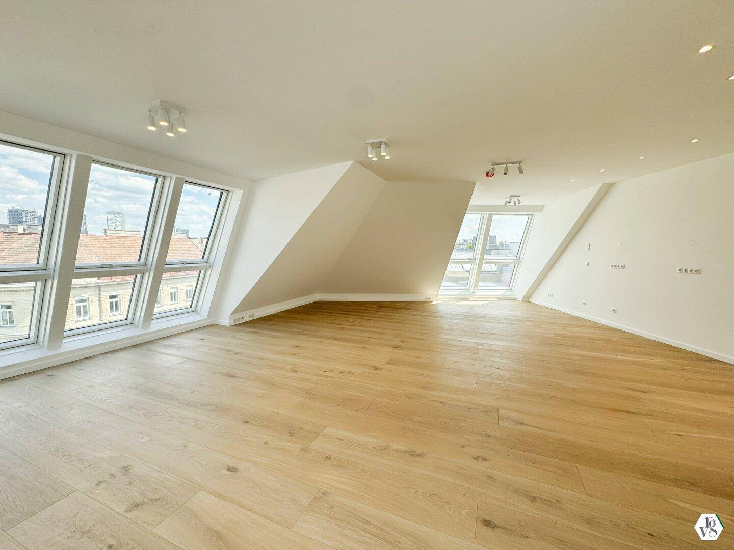 Großzügiger Wohnbereich im Dachgeschoss mit schrägen Wänden, Holzboden und viel Tageslicht.