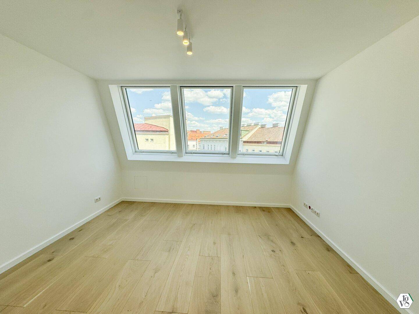 Helles Zimmer im Dachgeschoss mit schrägen Wänden, Holzboden und großen Dachfenstern.