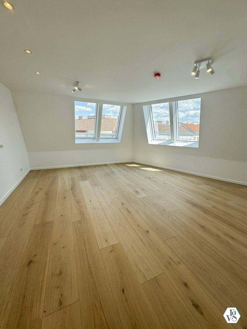 Lichtdurchflutetes Dachgeschosszimmer mit Holzboden, schrägen Wänden und mehreren Dachfenstern.