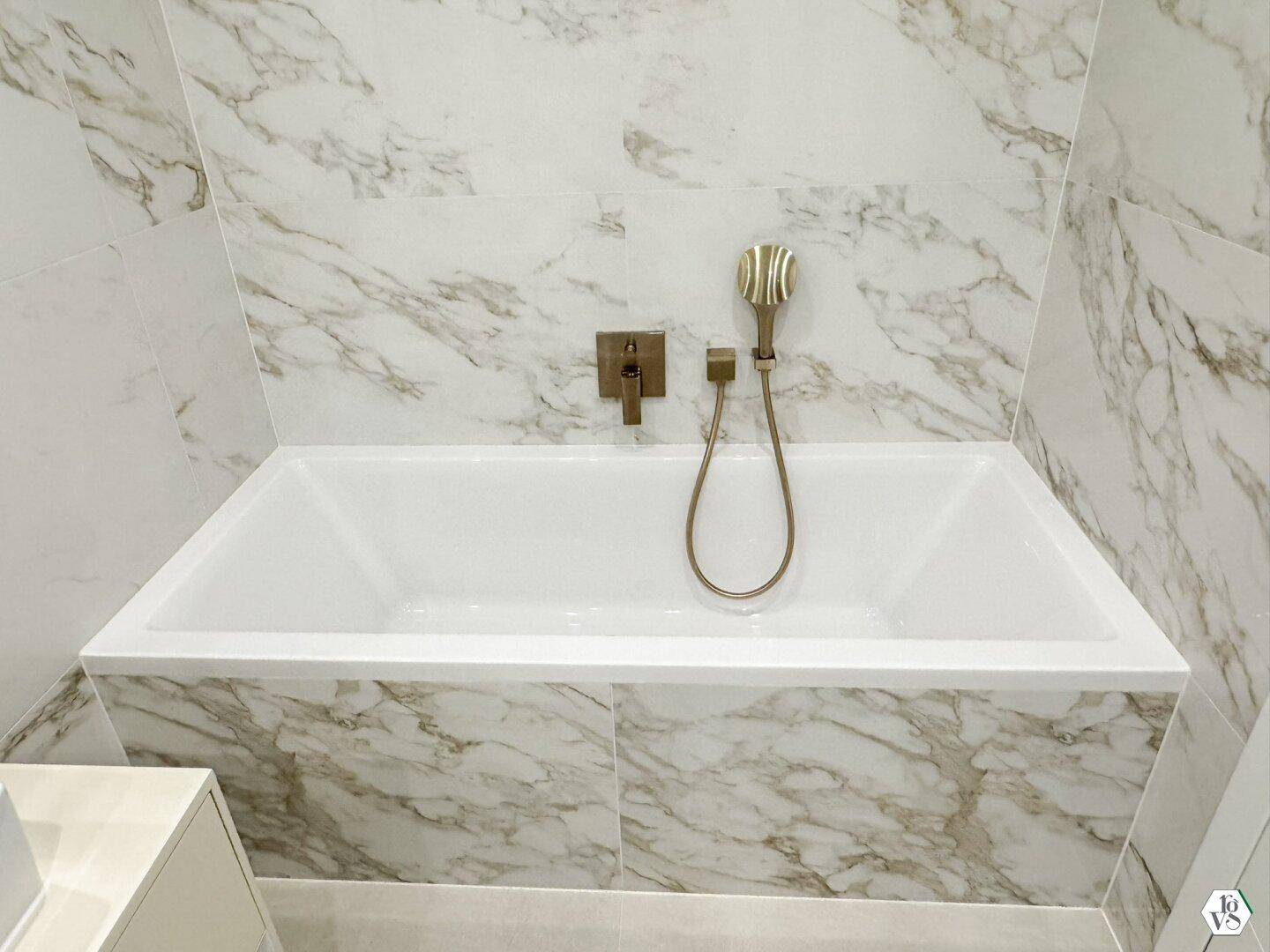 Moderne Badewanne mit eleganten Marmorfliesen und stilvollen Armaturen in Gold.