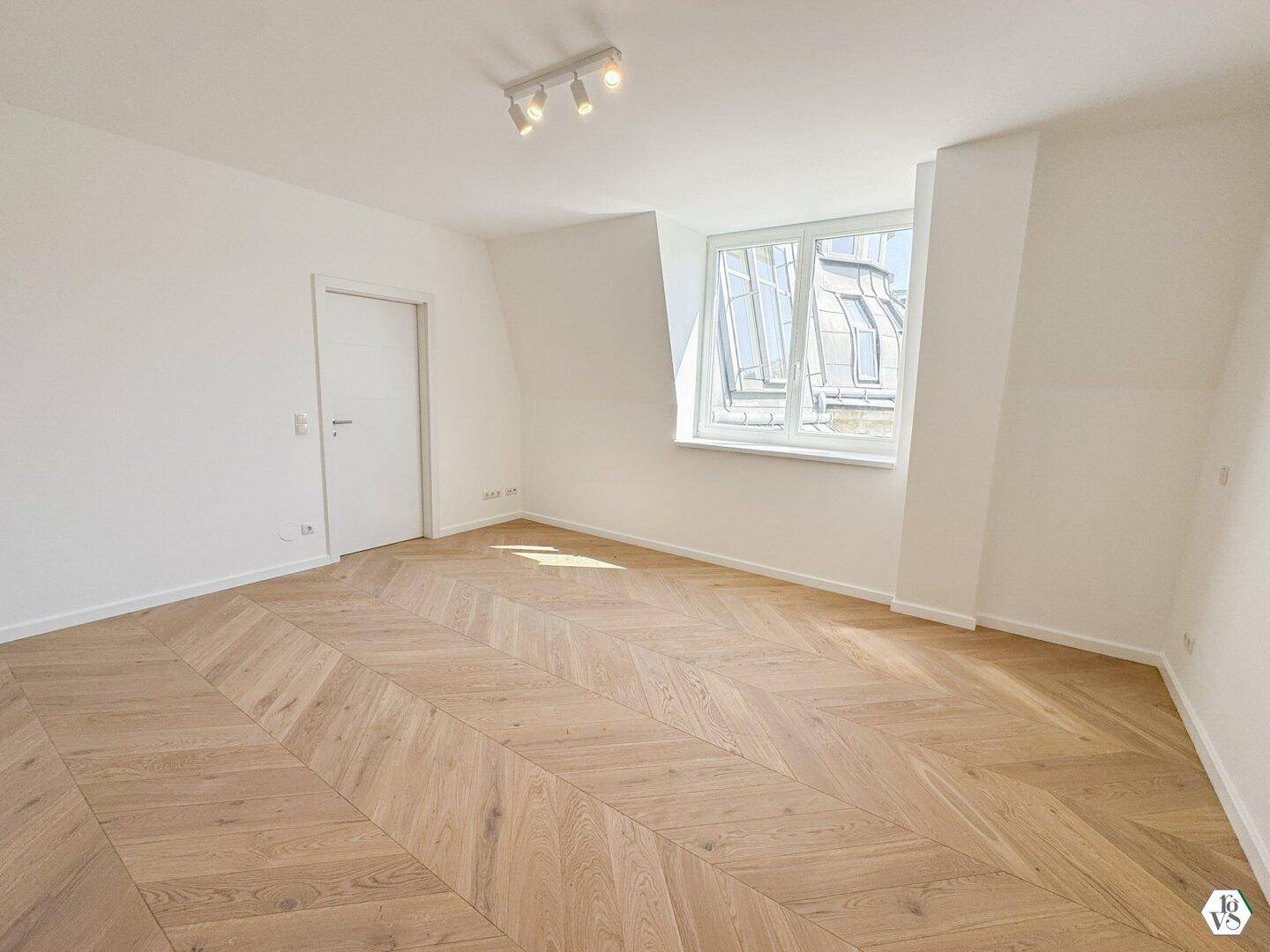 Helles Zimmer mit Fischgrätparkett, Dachschräge und großem Fenster.
