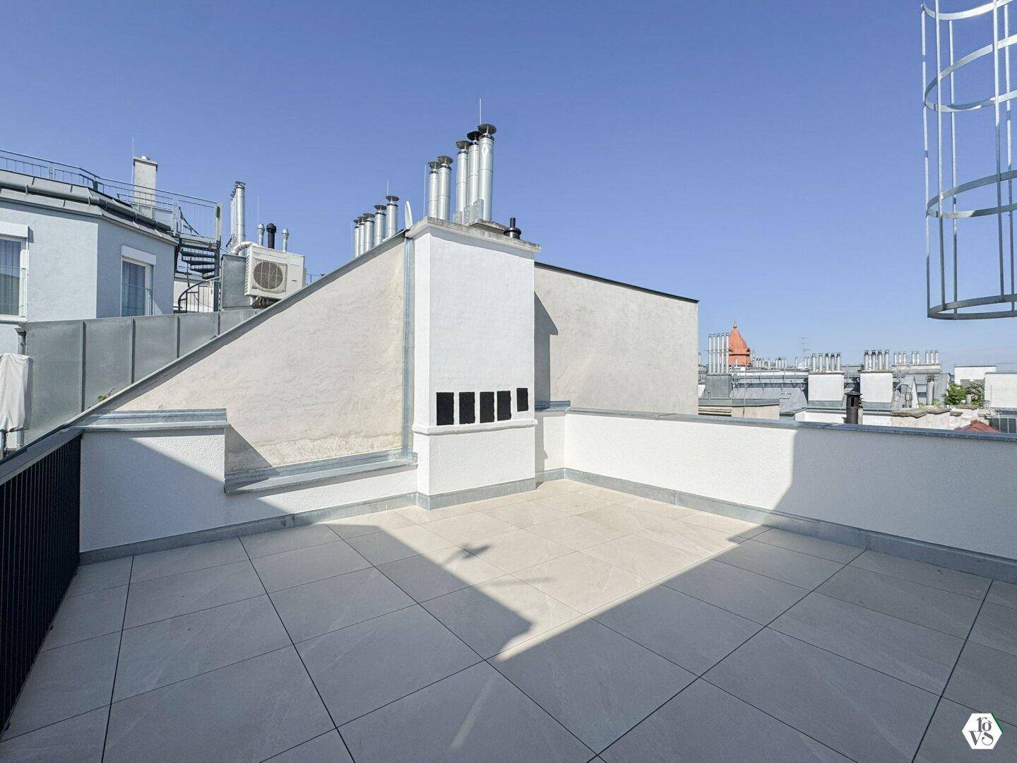 Geräumige Dachterrasse mit Fliesenboden und Blick über die Dächer der Stadt.