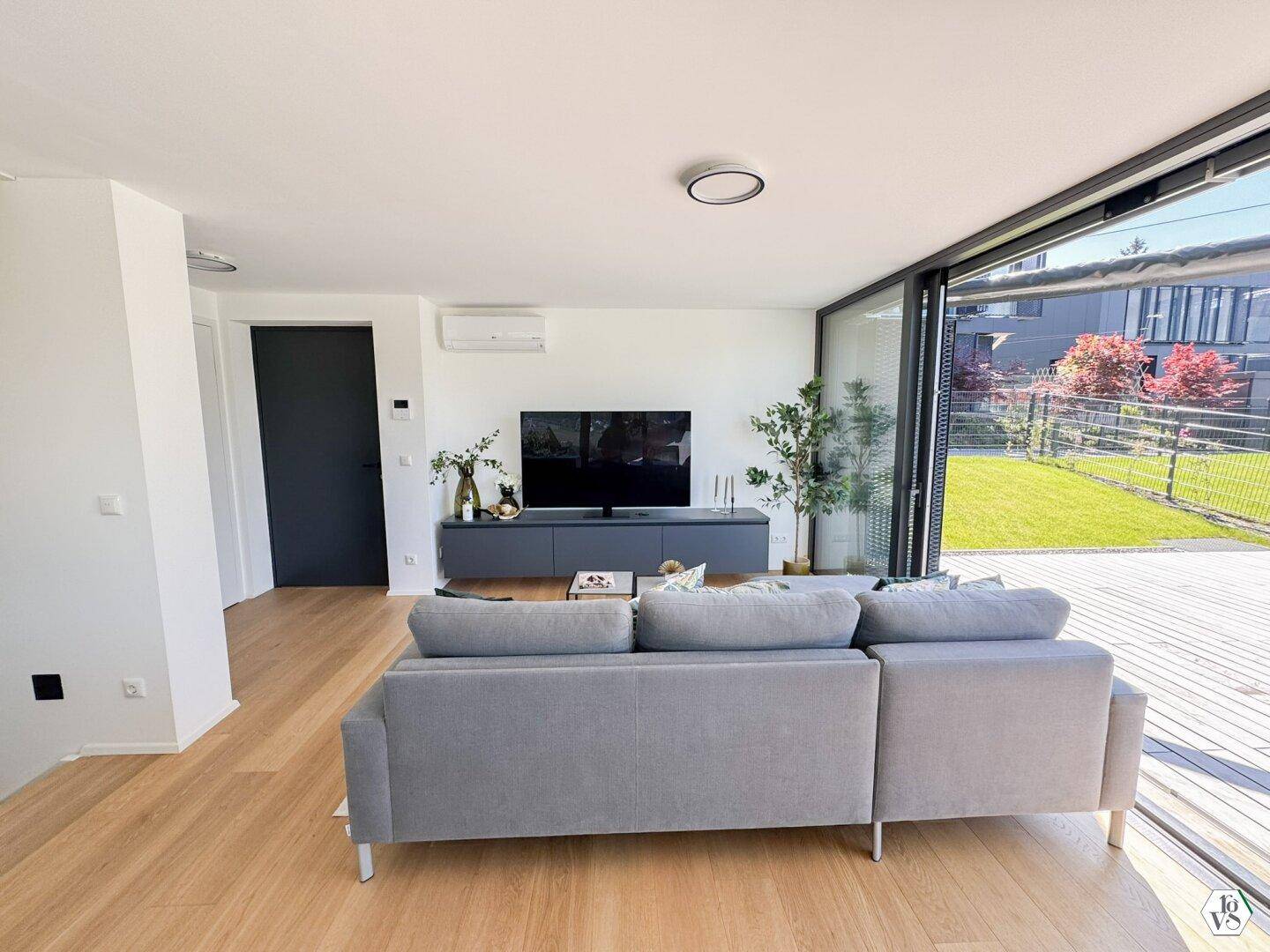 Helles Wohnzimmer mit Holzboden, großem Sofa und Zugang zur Terrasse.