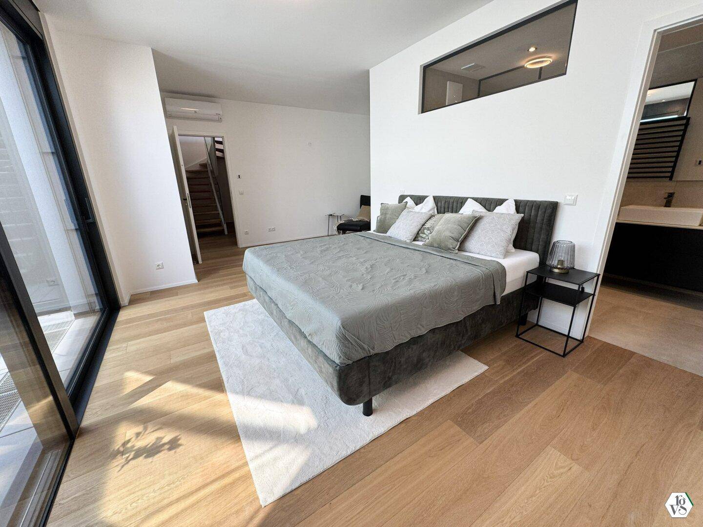 Schlafzimmer mit großem Bett, Holzboden und offenem Zugang zu einem angrenzenden Bad.