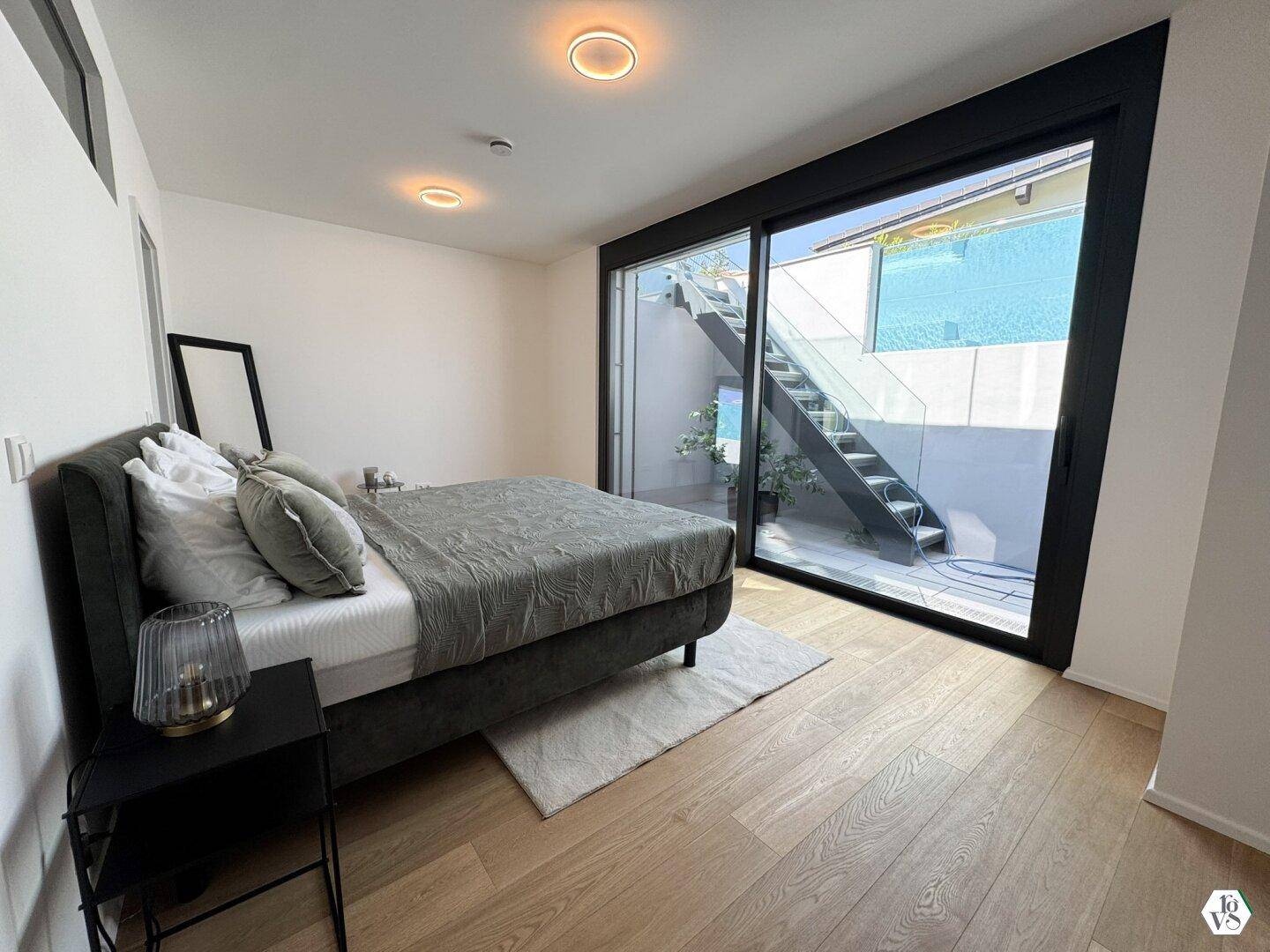 Schlafzimmer mit Holzboden und direktem Zugang zu einem Außenbereich über eine Treppe.