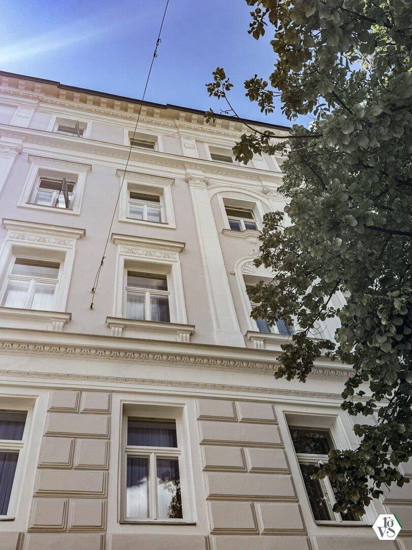 Historische Fassade eines Altbaus mit eleganten Verzierungen und hohen Fenstern unter blauem Himmel.