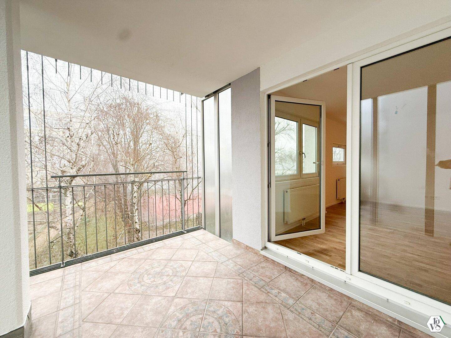 Geräumiger Balkon mit Fliesenboden und Blick ins Grüne.