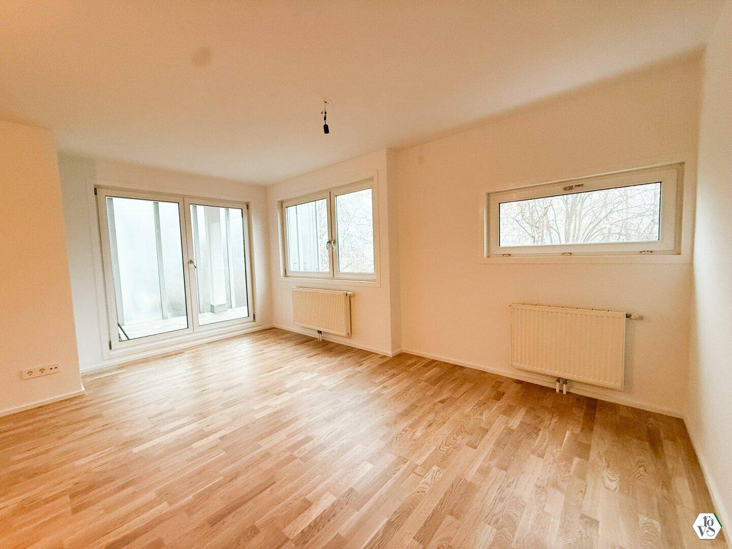 Heller Wohnbereich mit Parkettboden und großen Fenstern.