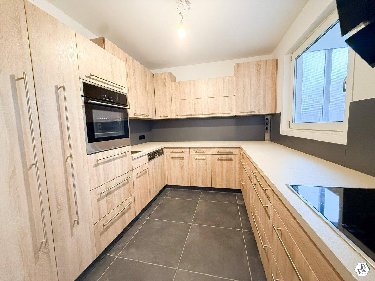 Moderne Einbauküche mit hellen Holzfronten, integrierten Geräten und Fenster.