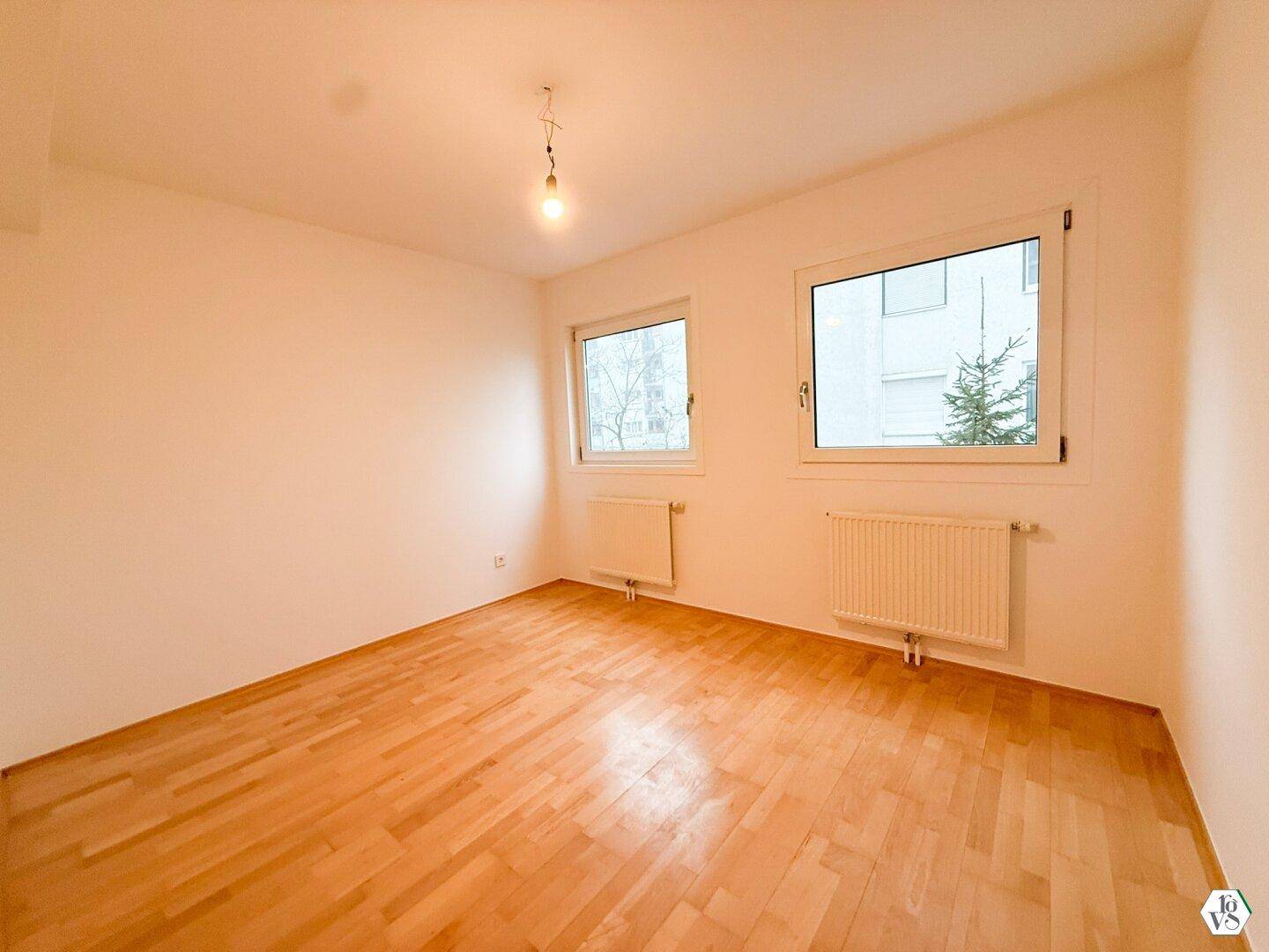 Helles Schlafzimmer mit Parkettboden und Blick ins Grüne.