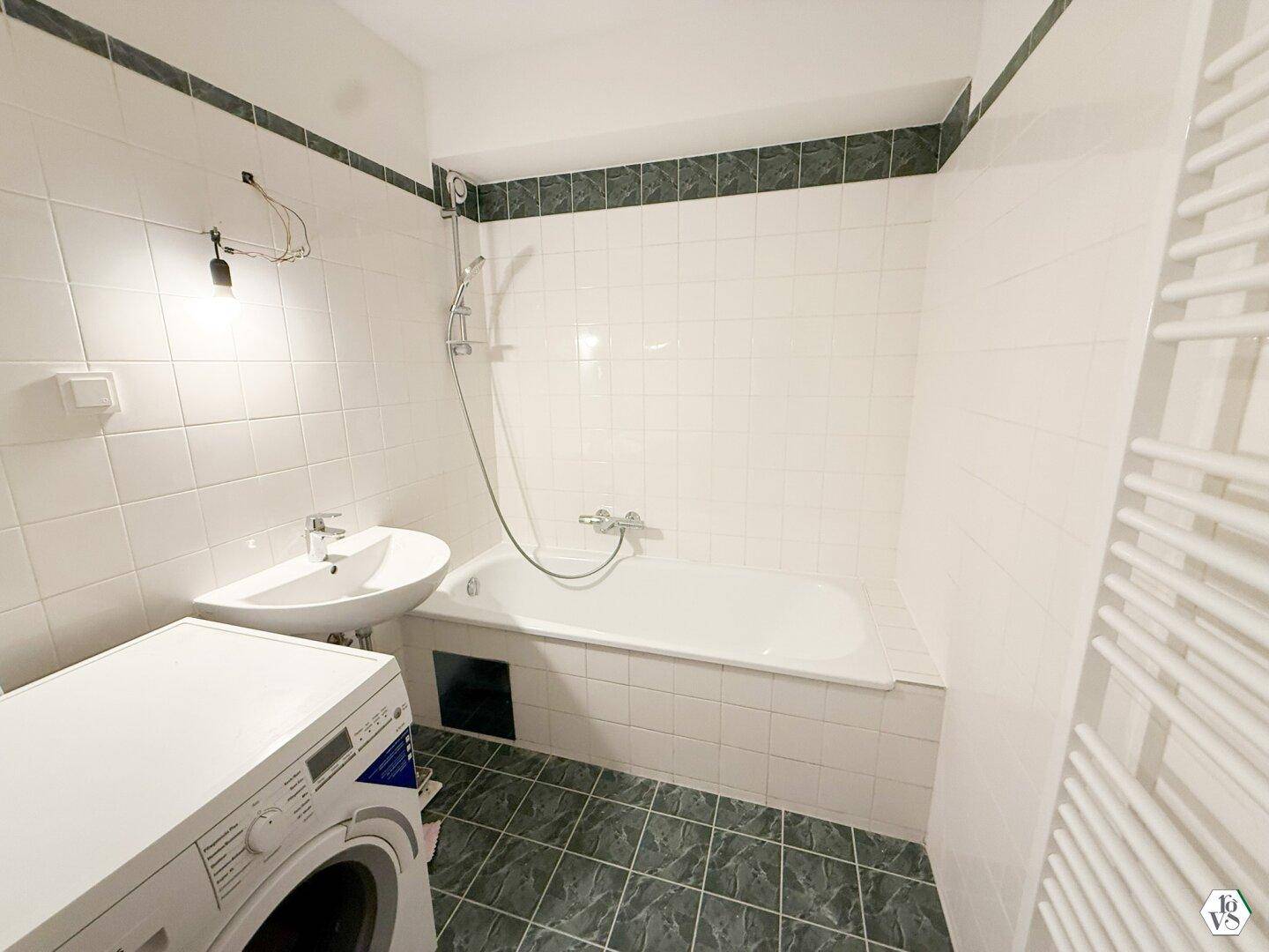 Badezimmer mit Badewanne, Waschbecken, beheiztem Handtuchhalter und Waschmaschine.