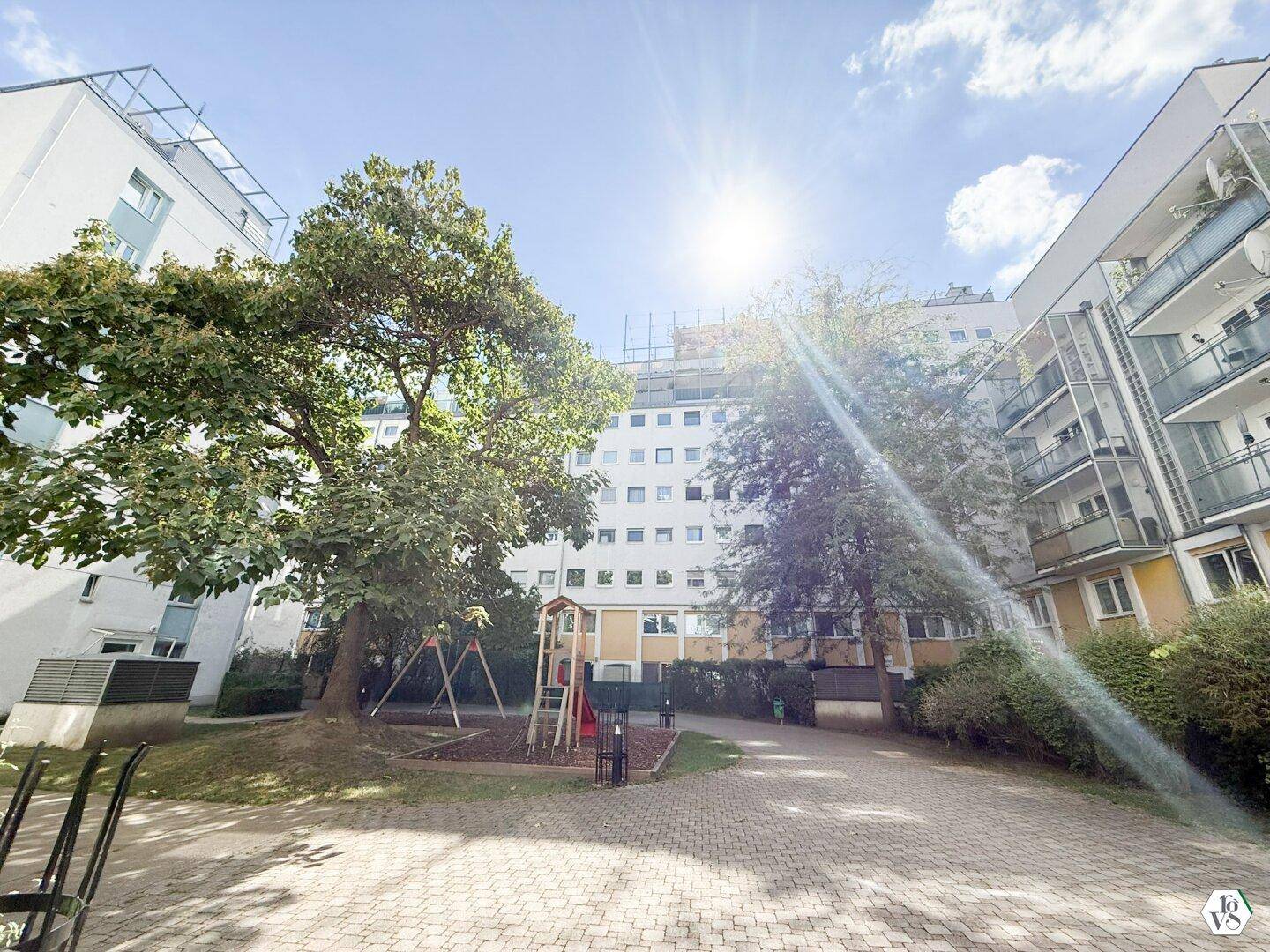Sonnenbeschienene Außenansicht des Wohngebäudes mit Spielplatz im Vordergrund.