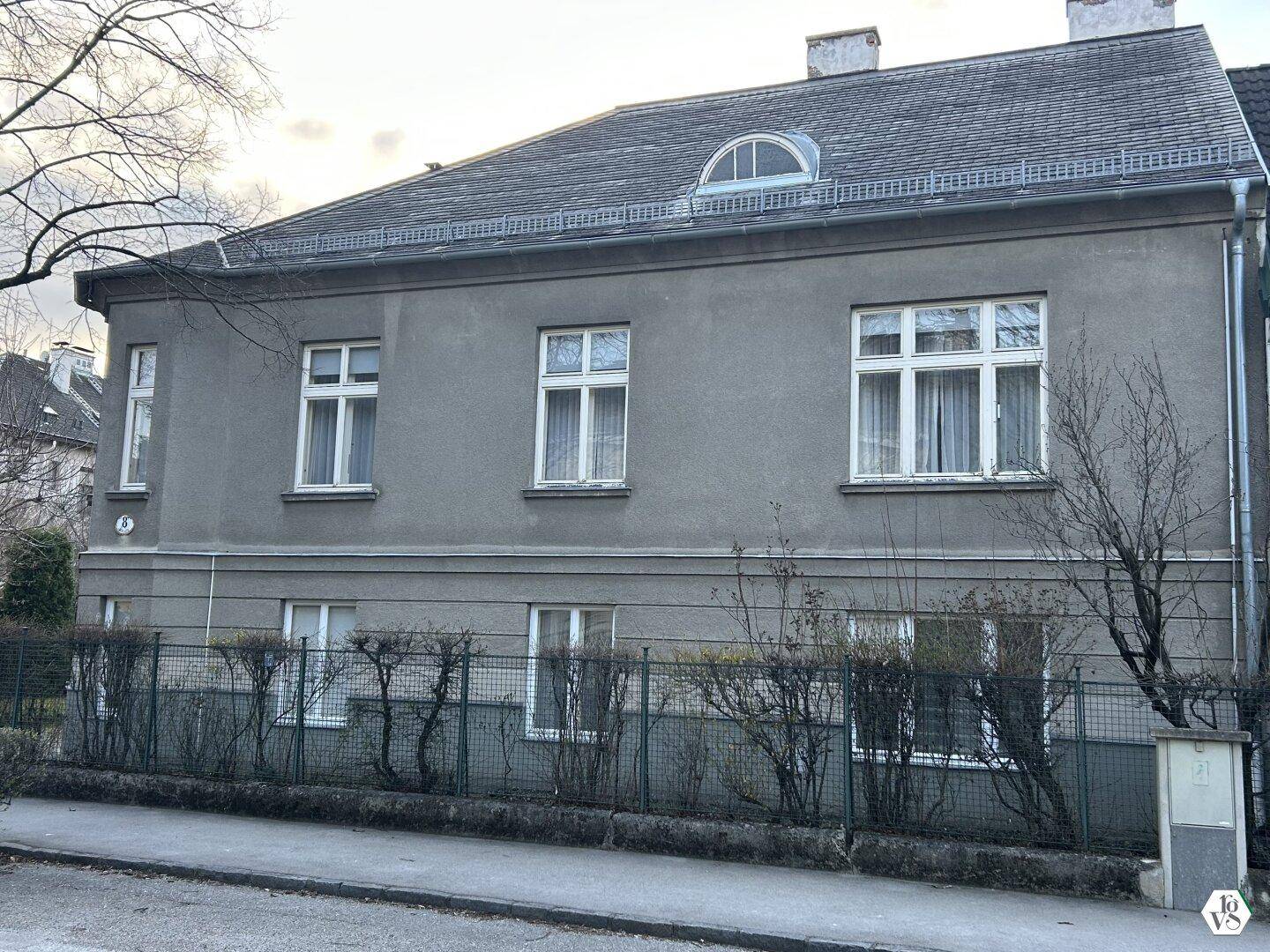 Klassisches Mehrfamilienhaus mit grauer Fassade, vielen Fenstern und einem Mansarddach.