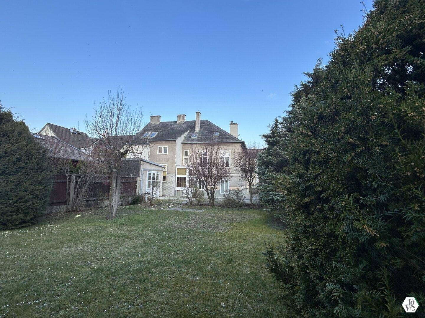 Großer Garten mit Rasen und hohen Hecken, der das klassische Wohnhaus im Hintergrund umgibt.