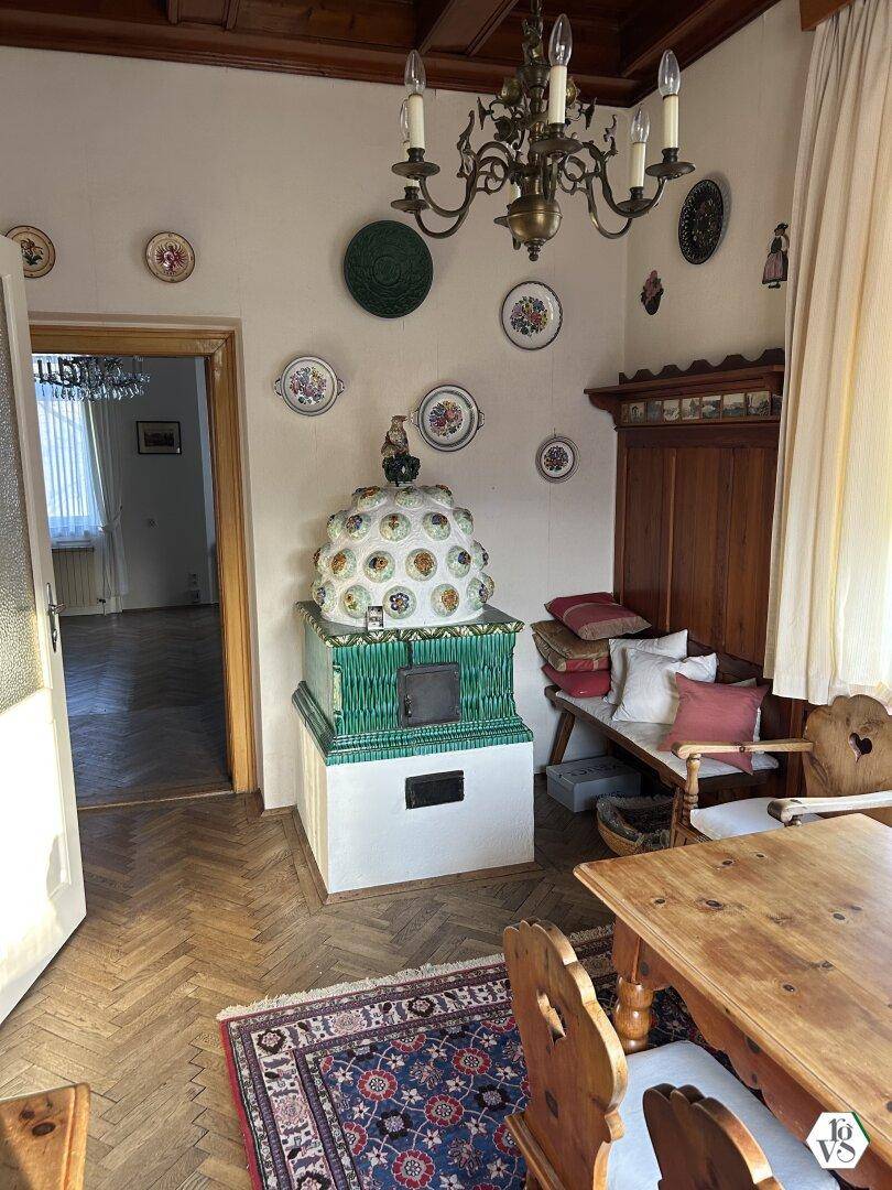 Traditionelles Esszimmer mit Kachelofen, Holztisch und dekorativen Tellern an den Wänden.