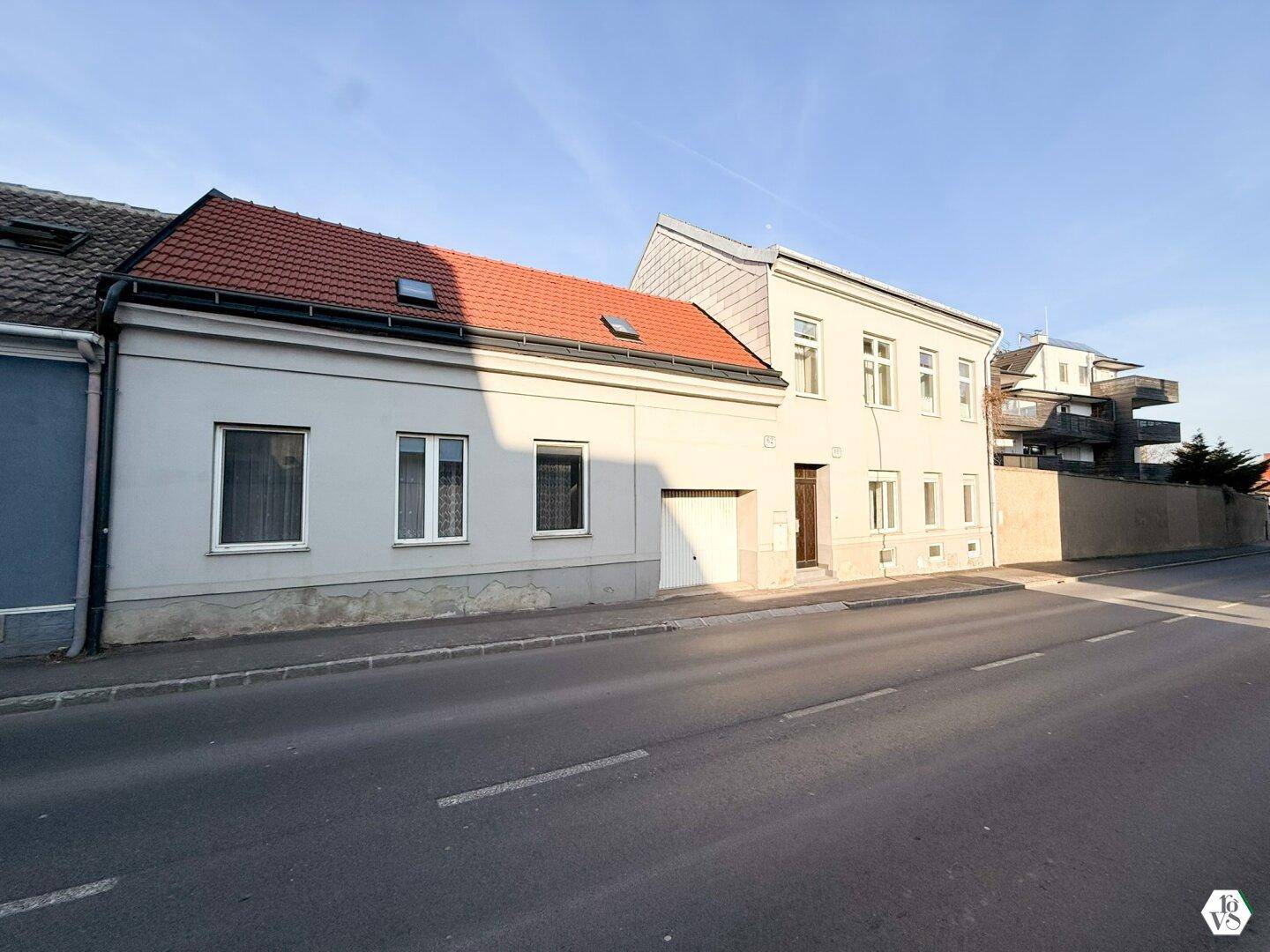Fassade eines Wohnhauses mit rotem Ziegeldach und Garageneinfahrt von der Straße aus.