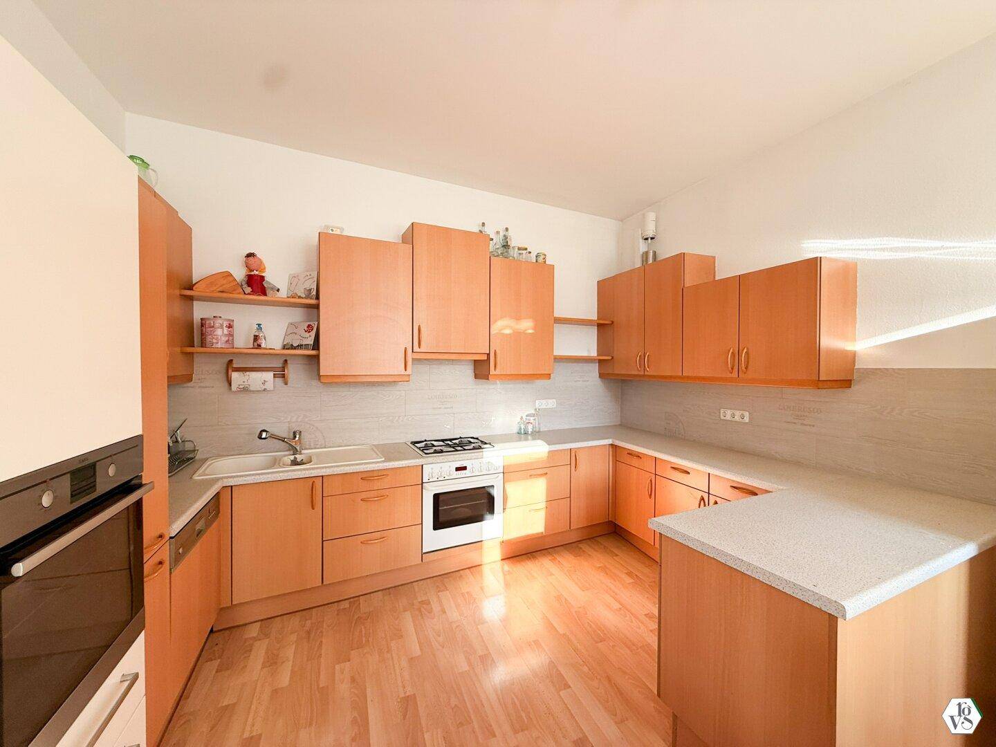Funktionale Küche mit hellen Holzschränken, weißer Arbeitsplatte und Gasherd.
