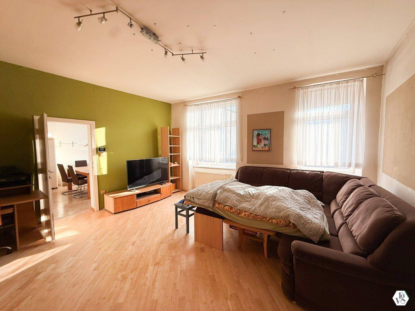 Helles Wohnzimmer mit braunem Sofa, grünem Akzentwand und hellem Parkettboden.