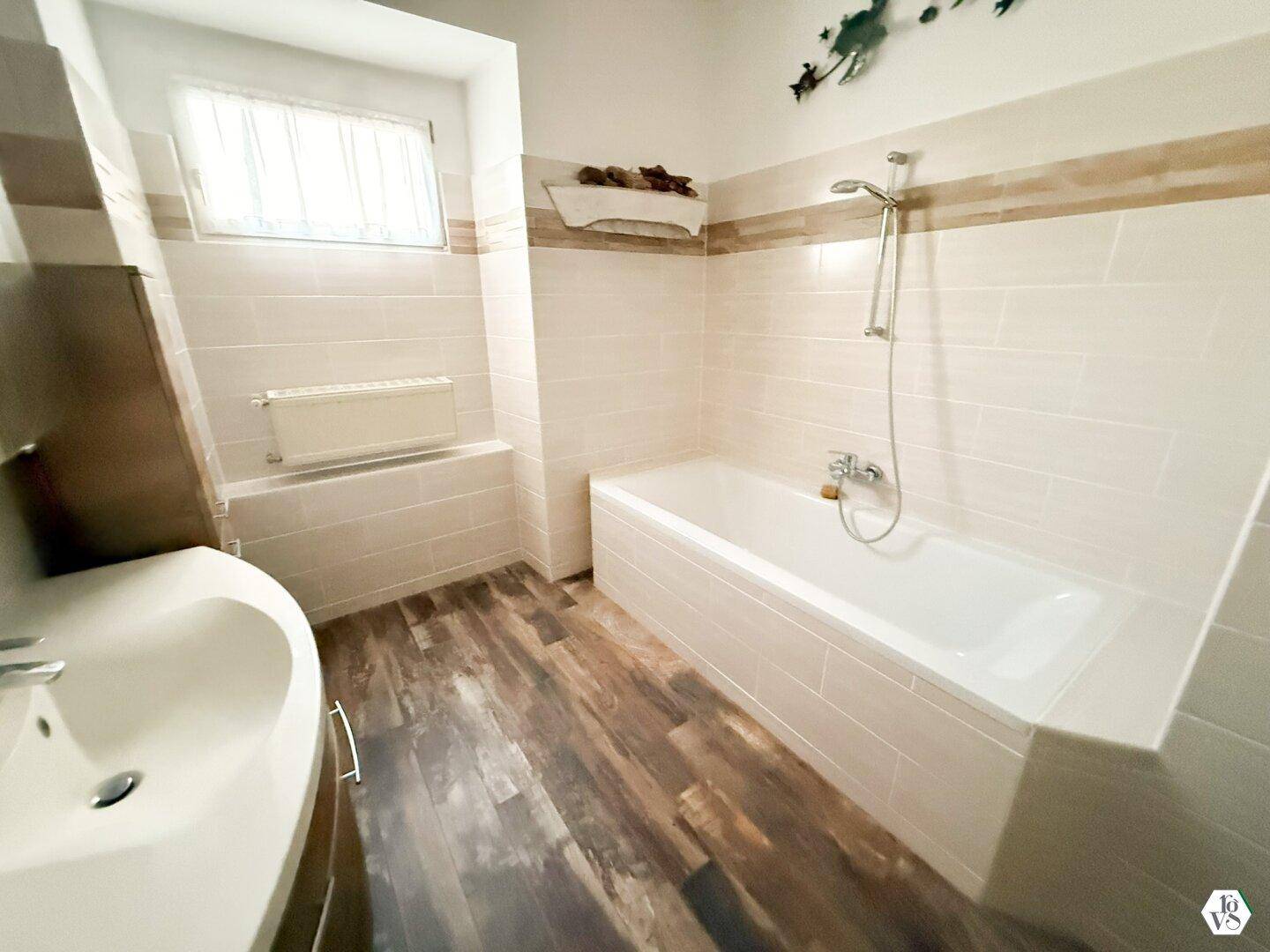 Badezimmer mit Badewanne, Waschbecken, Fenster und gefliesten Wänden.