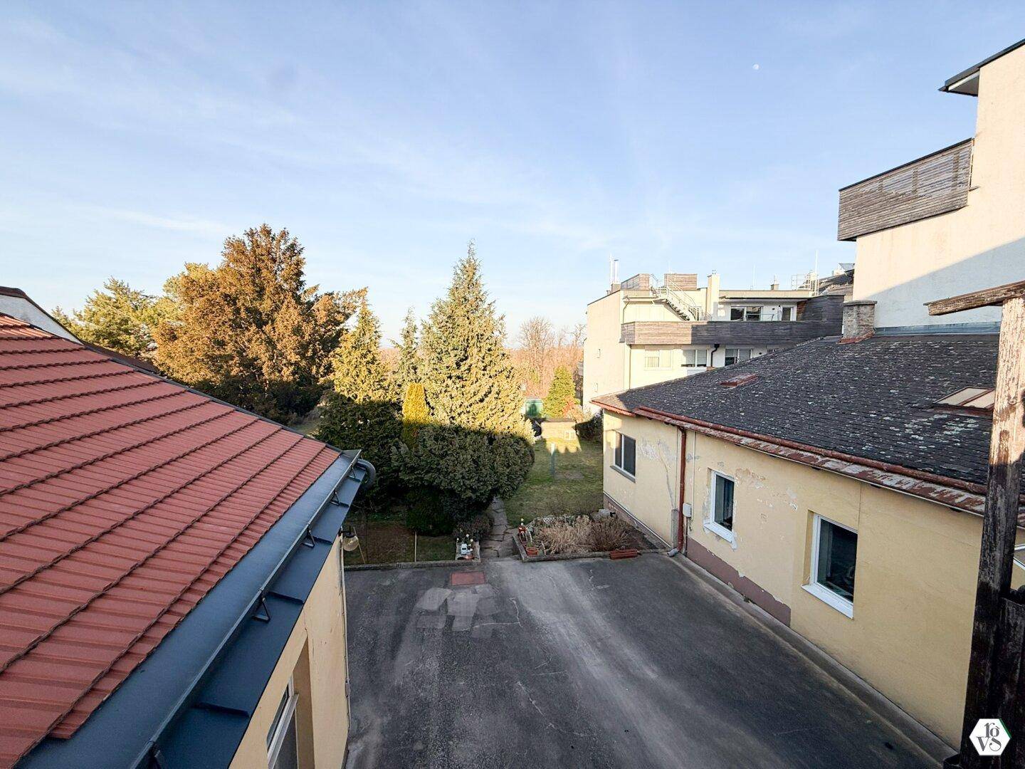 Blick von oben auf Dächer, einen Innenhof und dahinterliegende Grünflächen.