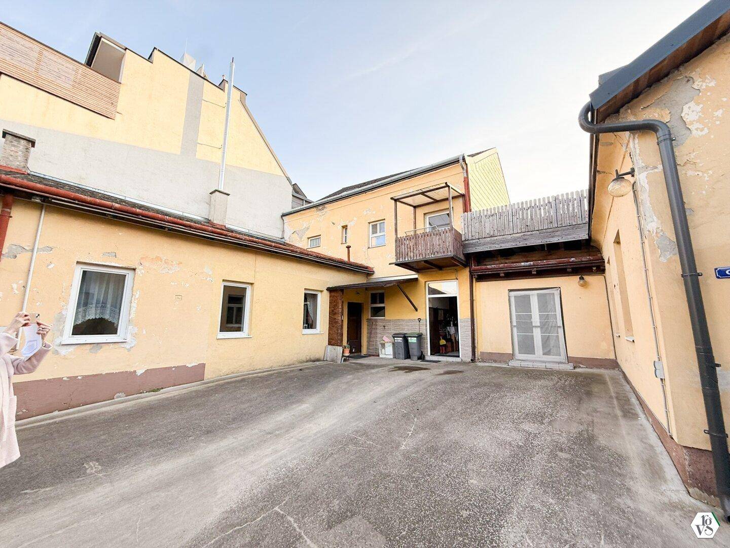 Innenhof mit gelben Gebäudefassaden, Betonboden und einem kleinen Balkon.