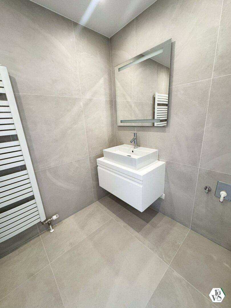 Modernes Badezimmer mit grauen Fliesen, Einzelwaschbecken und beheiztem Handtuchhalter.